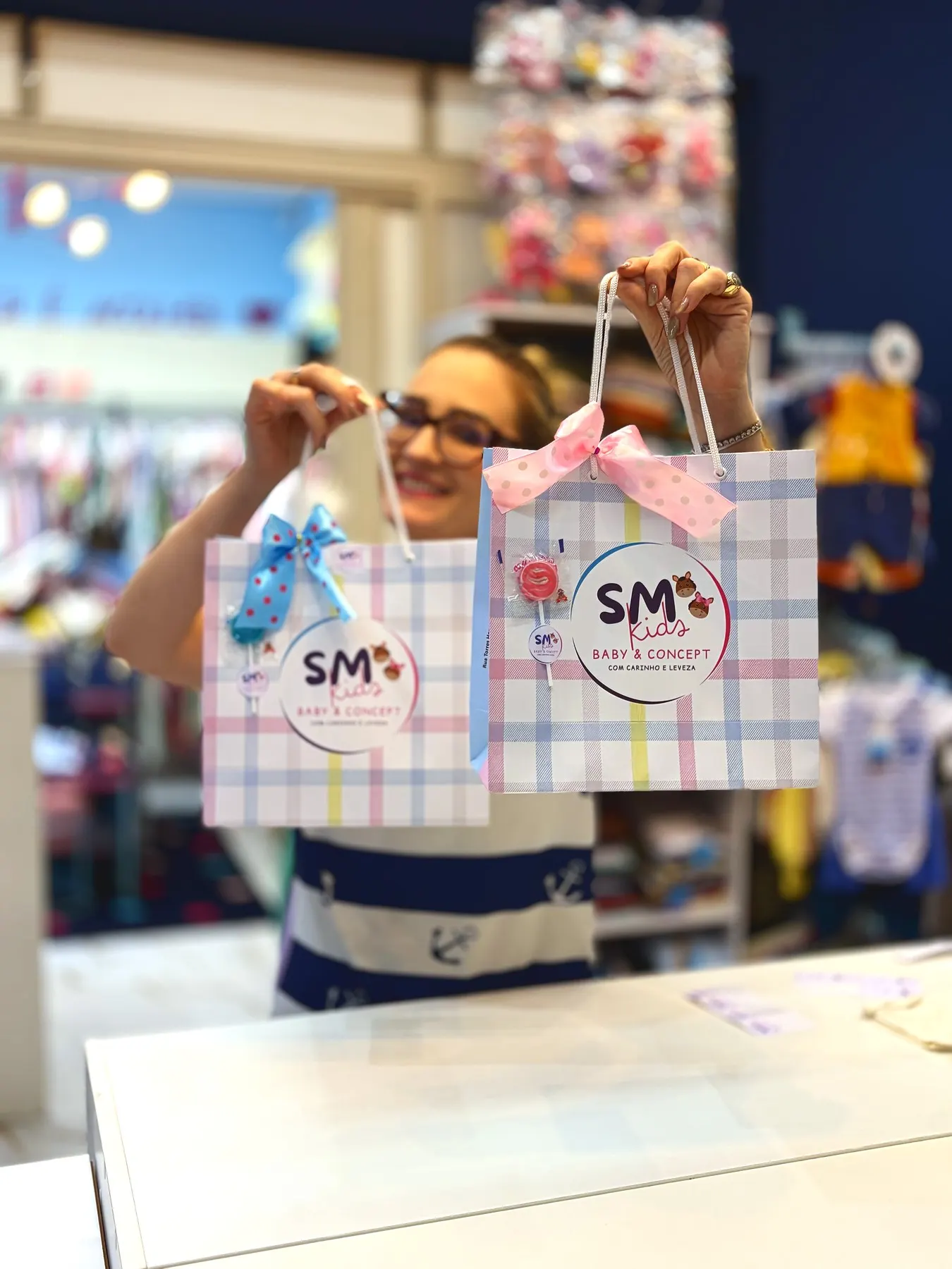 Atendente da SM Kids segurando duas sacolas de presente com laços rosa e azul dentro da loja